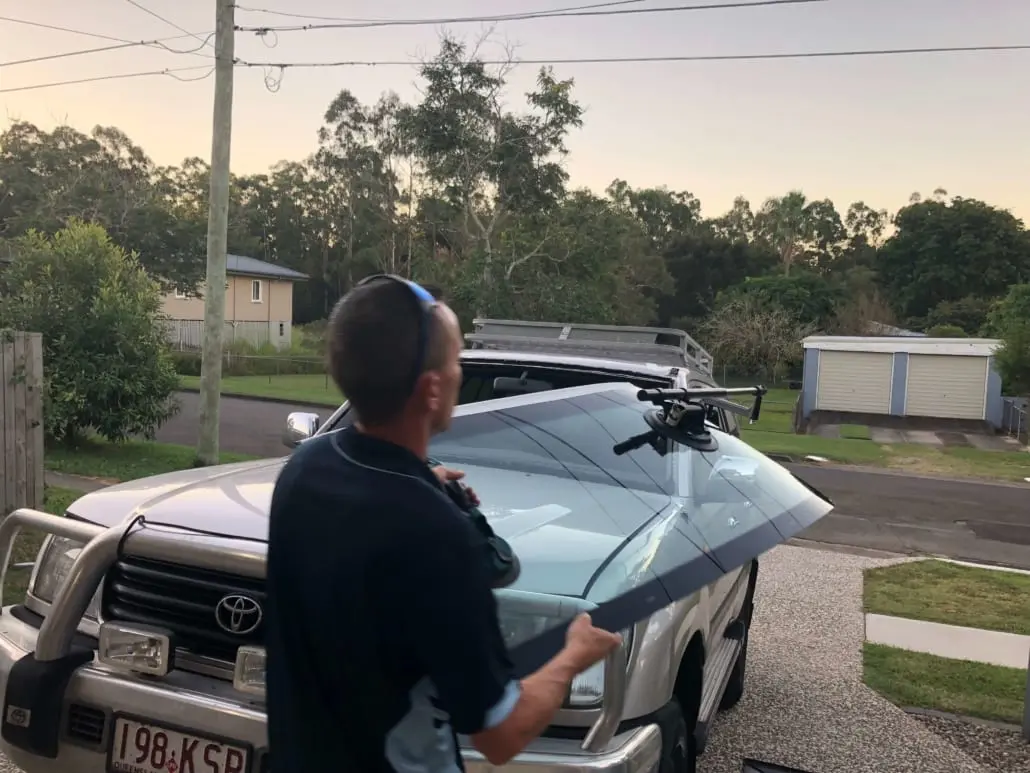 Technician carrying a new windscreen to a vehicle